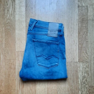 Replay Anbass Hyperflex jeans blå - Snygga blå Replay Anbass Hyperflex jeans med klassisk femficksdesign och raka ben. Jeansen har medelhög midja, diskreta slitningar och stretchigt material för extra komfort. Perfekta för dig som vill ha en modern och avslappnad look. byxornas storlek är 31 i midjan och 96cm långa