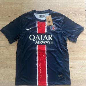 PSG O. Dembélé matchtröja Nike S - Paris Saint-Germain fotbollströja med O. Dembélé och nummer 10 på ryggen. Mörkblå bas med bred röd vertikal rand och vita detaljer. PSG-emblem och Nike-logga på bröstet, Qatar Airways som sponsor. Tillverkad i lätt och ventilerande material.