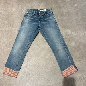 Levi's Vintage Orange Tab Limited Edition Jeans - Unika Levi's Vintage jeans, limited edition nr 341 av 409. Klassisk blå denim med snygga röda och vita randiga uppvik. Orange knapp och detaljer, raka ben och normal passform. Perfekta för dig som gillar retrostil och vill sticka ut med något ovanligt.