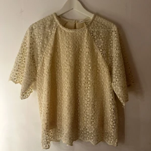 Beige spetsblus från InWear copenhagen  - Superfin beige blus från InWear med blommigt spetsmönster och korta ärmar. Blusen har rund halsringning och knapp i nacken. Perfekt för dig som gillar romantiska detaljer och en luftig känsla. Storlek L