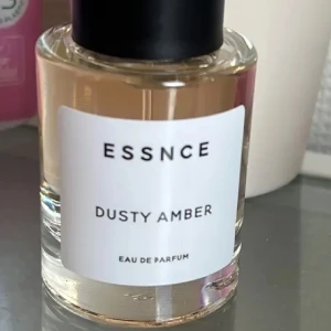 ESSNCE Dusty Amber Eau de Parfum - Parfymflaska från ESSNCE med doften Dusty Amber. Flaskan är rund och genomskinlig med svart lock och vit etikett. Testad en sprej 