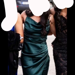 Mörkgrön  långklänning med slits - Säljer en elegant mörkgrön långklänning med en fallande halsringning och hög slits framtill. Klänningen är ärmlös och har en figurnära passform som framhäver siluetten. Perfekt för bal eller festliga tillfällen.