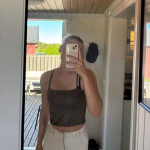 Mörkbrun croppad linnetopp med smala axelband - Säljer en mörkbrun croppad linnetopp med smala axelband och rak halsringning. Toppen är enkel och stilren, perfekt för varma dagar. Passar snyggt till både jeans och kjol.