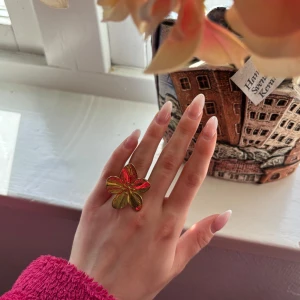 Blommig ring i guldfärg - Säljer en unik trendig ring i form av en blomma. Ringen är i guldfärg och har en justerbar öppning baktill. Perfekt för dig som vill ha ett statement-smycke med färg. Knappt använd och har inga defekter! Öppen för prisförslag🥰