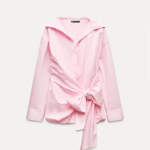 Oversized Ljusrosa skjorta med rosett från Zara - Säljer en ljusrosa skjorta från Zara med lång ärm och stor rosett framtill. Skjortan har klassisk krage, knappar och en snygg omlott-detalj som ger en trendig look. Perfekt för dig som vill sticka ut lite extra!
