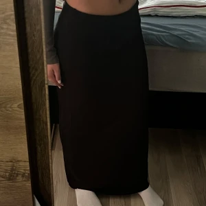 Svart långkjol från Cubus - Säljer en svart långkjol från Cubus. Kjolen har en enkel och stilren design med rak passform och resår i midjan. Perfekt att styla med crop tops eller stickade tröjor för en trendig look.