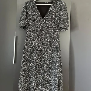 🌸Blommig klänning🌸 - Säljer en svart klänning med små vita och ljusrosa blommor, v-ringning och puffärmar. Klänningen har knäppning vid ärmslut och är i ett lätt, luftigt material. Perfekt för vår och sommar! Storlek XS💗🌸