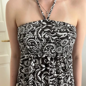 Brun och vit halternecktopp med mönster - Säljer en brun och vit halternecktopp med smock upptill och ett snyggt paisleyinspirerat mönster. Toppen  har tunna axelband som knyts i nacken och en luftig passform, perfekt för varma dagar. Är storlek M men passar XS - L