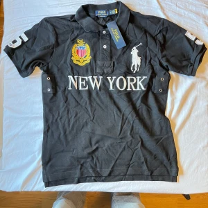 Chief keef polo - Säljer en svart pikétröja från Polo Ralph Lauren med broderad logga, New York-tryck och emblem på bröstet. Nummer 5 på ryggen och ärmarna. Klassisk krage och knappar framtill. Perfekt för en sportig och stilren look.