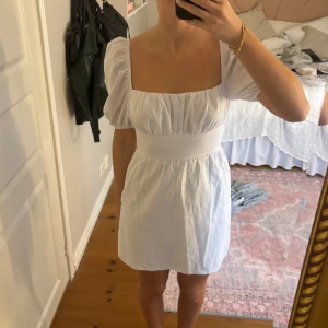 Vit kortklänning med puffärm från Hello Molly - Supersöt vit kortklänning från Hello Molly med puffärmar, fyrkantig ringning och stor rosett i ryggen. Klänningen har smock i midjan och är tillverkad i ett lätt bomullstyg. Perfekt för studenten! Köpte för 1100 kr, aldrig använd.