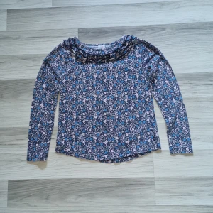 Blommig långärmad tröja från Polarn O. Pyret - Säljer en söt långärmad tröja från Polarn O. Pyret i storlek 134/140. Tröjan är blå med blommigt mönster i rosa och vitt samt har volangdetaljer vid halsen. Perfekt för dig som gillar färg och mönster!