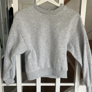 Ljusgrå sweatshirt - En basic ljusgrå sweatshirt med rund halsringning och ribbade muddar vid ärmslut och nederkant. Tröjan har en avslappnad passform och är perfekt för en enkel och stilren look.