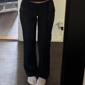 Svarta kostymbyxor - Snygga svarta kostymbyxor med hällor för bälte. Byxorna har fickor fram och dekorfickor bak.