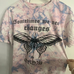 Tie-dye t-shirt med fjäril och text från FB Sister - Pastellrosa och blå tie-dye t-shirt från FB Sister med svart tryck av en stor fjäril och texten 'Sometimes we need changes' på bröstet. T-shirten har rund hals och korta ärmar. Perfekt för en cool och avslappnad stil.