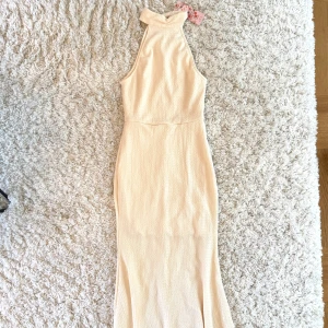 Champagnefärgad långklänning  - Säljer en elegant champagnefärgad långklänning från SHEIN MOD. Klänningen har hög hals med pärlknappar i nacken och är ärmlös. Materialet är strukturerat och ger en lyxig känsla. Perfekt för speciella tillfällen!