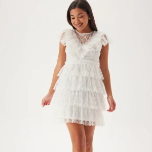 Bubbleroom klänning - Superfin vit kortklänning med flera lager volanger och spetsdetaljer. Klänningen har v-ringning och är ärmlös med romantisk känsla. Perfekt för sommarens tillfällen eller studentfirande. Söt och feminin design. Använd 2 gånger