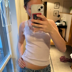 Ljuslila vintage ribbad linnetopp med spets - Säljer en ljuslila ribbad linnetopp med fina spetsdetaljer längs urringningen och axelbanden. Toppen är figurnära och har en mjuk, stretchig känsla. Perfekt att styla med jeans eller kjol.