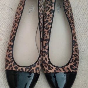 Leopardmönstrade ballerinaskor med lackad tå - Säljer ett par ballerinaskor från Rizzo med leopardmönster och svart lackad tå. Skorna har rund tå och platt sula, perfekta för dig som vill sticka ut lite extra.