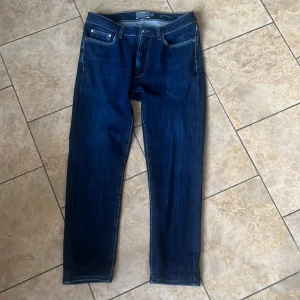 Mörkblå jeans från Dressmann - Säljer ett par klassiska mörkblå jeans från Dressmann. De har fem fickor, raka ben och normal passform. Perfekta för dig som gillar en tidlös stil och vill ha ett par bekväma jeans till vardags.