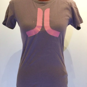 Lila t-shirt med rosa tryck från WESC S - Lila t-shirt från WESC med ett stort rosa grafiskt tryck på bröstet. Klassisk rund halsringning och korta ärmar. Tillverkad i mjuk bomull som känns skön mot huden. Perfekt för en avslappnad och cool stil.  100% bomull  Litet hål vid halsen! Längd: 35 cm