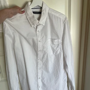 Vit skjorta med knappar - Klassisk vit skjorta med lång ärm och knappar framtill. Skjortan har en bröstficka och en stilren krage, perfekt för en clean och enkel look. Passar till många olika outfits och är ett måste i garderoben.