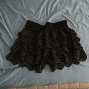Svarta virkade shorts med volang - Säljer ett par svarta virkade shorts med flera lager volang och bred resår i midjan. De har en feminin och bohemisk känsla och är perfekta för sommardagar. Superfina detaljer i virkningen och sköna att bära.