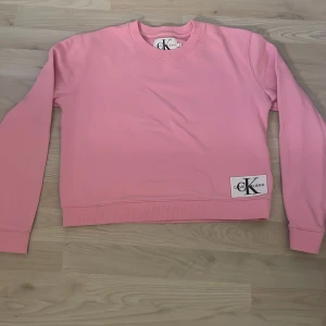Rosa sweatshirt från Calvin Klein Jeans - Säljer en ljusrosa sweatshirt från Calvin Klein Jeans. Tröjan har rund halsringning, långa ärmar och en ribbad mudd vid ärmslut och nederkant. CK-logga sitter framtill nere vid fållen. Perfekt för en avslappnad stil!