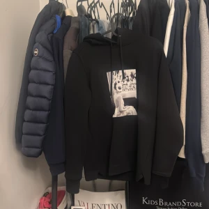 Svart hoodie med tryck från Ellen von Unwerth - Säljer en svart hoodie med ett unikt svartvitt tryck framtill som föreställer en person med kaninmask. Tröjan har huva med dragsko och en avslappnad passform. Perfekt för dig som gillar statement-plagg och coola motiv.