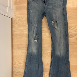Blå bootcut jeans från Hollister - Säljer ett par blå bootcut jeans från Hollister med slitna detaljer på framsidan. Jeansen har klassisk femficksdesign och normal passform. Skriv för fler bilder eller frågor!