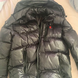 Svart pufferjacka från Polo Ralph Lauren - Säljer en svart pufferjacka från Polo Ralph Lauren med röd broderad logga på bröstet. Jackan har huva, dragkedja framtill och två dragkedjefickor. Perfekt för kyliga dagar och riktigt snygg streetstil.