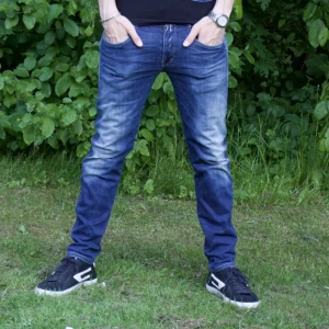 Replay Anbass  - Snygga blå slim fit jeans med klassisk femficksdesign och tydliga slitningar på låren. Jeansen har normal midja och raka ben med lätt tvättad effekt. Perfekta till sneakers och t-shirt för en avslappnad look. 33/32 Anbass. Hål på höger knä!