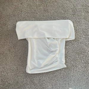 Vit offshoulder tubtopp - Säljer en vit offshoulder tubtopp från Dazy. Toppen har en stilren och enkel design med bred kant upptill och är axelbandslös. Perfekt för dig som gillar minimalistiska plagg och vill ha något snyggt till sommaren.