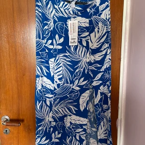 Blåvit långklänning med bladmönster - Säljer en blå långklänning med vitt bladmönster. Klänningen har en luftig passform och är ärmlös, perfekt för varma dagar. Materialet är lätt och känns svalt mot huden. Snygg att styla med sandaler eller sneakers.