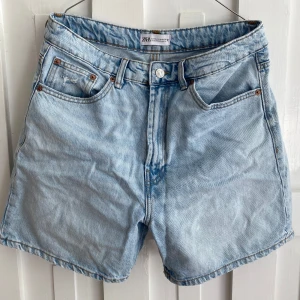 Ljusblå jeansshorts från ZARA - Ljusblå jeansshorts från ZARA med klassisk femficksdesign och normal passform. Shortsen har hög midja och är tillverkade i denim med synliga sömmar och knappgylf.