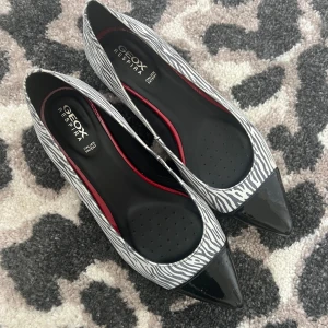 Zebramönstrade ballerinaskor från Geox - Säljer ett par snygga ballerinaskor från Geox med zebramönster och spetsig tå. Skorna har svart lackdetalj framtill och en klassisk klack. Perfekta för dig som vill sticka ut med ett djurmönster och elegant design. De har en liten slitning framtill, men inget som egentligen syns på långt håll. Endast använd en gång då de är för stora för mig 💔Storlek 38,5. Jag är öppen för prisförslag 