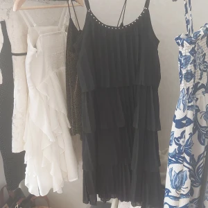 Svart volangklänning med nitar från KappAhl - Säljer en svart klänning från KappAhl med volanger i flera lager och dekorativa nitar längs den rundade urringningen. Klänningen har smala axelband och ett luftigt, flowy fall. Perfekt för dig som gillar en stilren men ändå detaljrik look. Helt oanvänd!