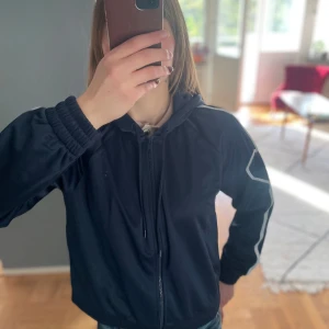 Mörkblå sportig vindjacka med vita detaljer från Monki - Säljer en mörkblå vindjacka/zip hoodie från Monki med huva och vita vågiga detaljer längs ärmar och framsida. Jackan har dragkedja, resår vid ärmslut och nederkant samt en sportig look. Perfekt för dig som gillar streetwear. Oanvänd med lappar kvar. 