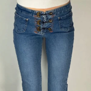 Blå bootcut jeans med unika knappar - Säljer ett par blå bootcut jeans med låg midja och snygga dekorativa knappar framtill. Jeansen har klassiska fickor och är tillverkade i denim. Perfekta för dig som vill sticka ut med en cool detalj i vardagslooken.🥰(Jag är 172cm lång) Skriv om ni undrar något. Skickar ut paket samma dag om du köper innan klockan 21.
