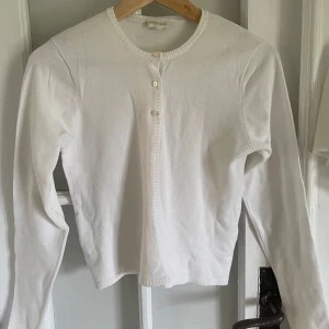 Vit kofta från POMPdeLUX - Säljer en klassisk vit kofta från POMPdeLUX i storlek 152. Koftan har rund halsringning, långa ärmar och knäppning med tre knappar framtill. 