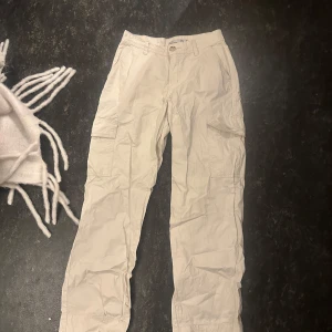 Beiga cargopants med fickor - Säljer ett lågmidjade par beiga cargopants med flera praktiska fickor på sidorna och baktill. Byxorna har normal passform, knapp och dragkedja framtill samt bälteshällor. Perfekta för en avslappnad och trendig stil.