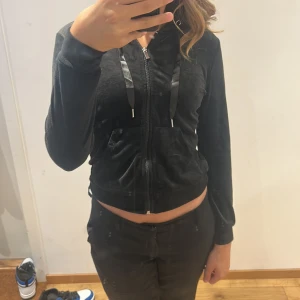Svart hoodiejacka från Gina Tricot - Säljer en svart hoodiejacka från Gina Tricot i storlek XS. Tröjan har dragkedja framtill, huva med snören och fickor på magen. Materialet är mjukt och har en lätt glansig finish på vissa detaljer.