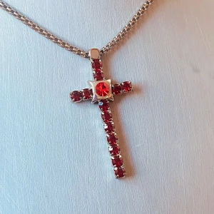Halsband med korshänge och röda stenar - Snyggt halsband med ett korsformat hänge dekorerat med röda stenar och en större röd sten i mitten. Kedjan är i silverfärg och har justerbar längd. Perfekt för dig som vill ha ett statement-smycke med färg.