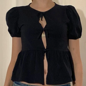Mörkblå blus med puffärm från Gina Tricot - Säljer en söt mörkblå blus från Gina Tricot med puffärmar och knyt framtill. Blusen har en lätt utsvängd nederdel och korta ärmar. Perfekt för dig som gillar en feminin och trendig stil.