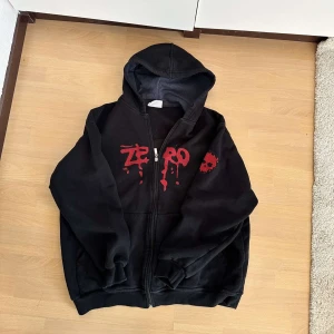 Svart zip-up hoodie med röd print - Svart oversized hoodie från Zero B*llshit med röd, droppande logga och döskalle på bröstet och ryggen. Köpt på second hand i Malmö men har använt ca 1 elr 2 gånger. Skulle säga att den är strl M/L 💘Kontakta gärna!