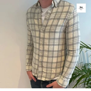 Ralph laurent skjorta - Snygg rutig skjorta i grått och beige med klassisk krage och knäppning framtill. Skjortan har lång ärm och en slim passform som sitter tajt mot kroppen. Perfekt att bära över en t-shirt för en avslappnad look.