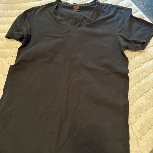 Svart v-ringad t-shirt från Levi's - Svart t-shirt från Levi's med v-ringad hals och korta ärmar. Enkel och stilren design som funkar till det mesta. Tillverkad i mjuk bomull för skön känsla hela dagen. Perfekt för dig som gillar klassiska plagg med en modern touch.