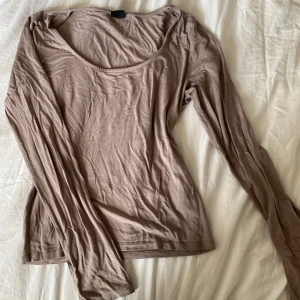Beige långärmad topp Gina Tricot - Supermjuk och tunn beige långärmad topp från Gina Tricot i storlek M men ganska liten i storlek. Modellen har en djup rundad halsringning och sitter slim på kroppen. Perfekt att styla med jeans eller shorts för en chill look. Materialet är stretchigt och känns skönt mot huden.