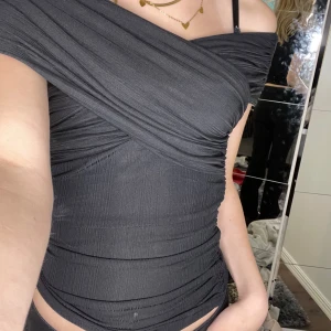 Svart offshoulder topp från Vila - Säljer en svart offshoulder topp från Vila i storlek XS. Toppen har en tight passform med snygga draperade detaljer och ribbad struktur. Kommer inte till användning därför säljer jag den!