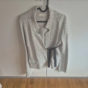 Mönstrad cardigan jacka med bälte - Superfin ljusgrå kofta från Odd Molly med snyggt mönster och svart knytbälte i midjan. Jackan har lång ärm, mjukt material och avslappnad passform. Perfekt för lager-på-lager och chill vibes.