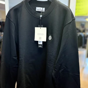 Svart sweatshirt från Stone Island - Har alla storlekar.  Svart sweatshirt från Stone Island med klassisk rund hals och logopatch på bröstet. Tröjan har lång ärm och är tillverkad i mjuk bomull. Perfekt för dig som gillar stilrena och enkla plagg med exklusiv känsla. Passar dig som vill ha en clean look.